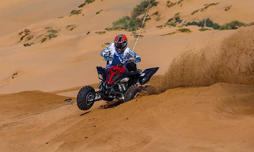 Guest riding Yamaha Raptor over red sand dunes